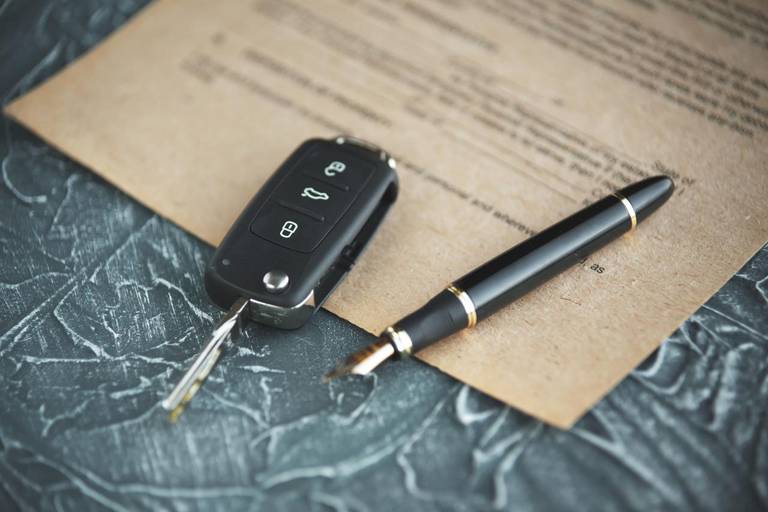 Black car key and money on a signed contract of car sale. Focus on a key.