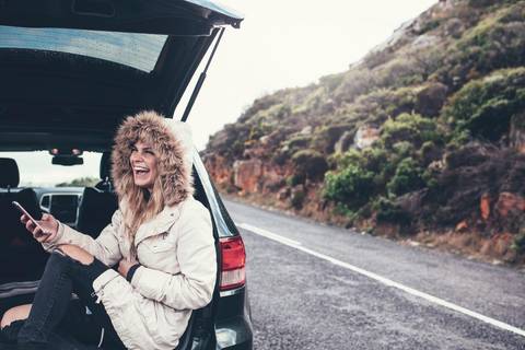 Woman sitting in trunk of car with smartphone in her hand