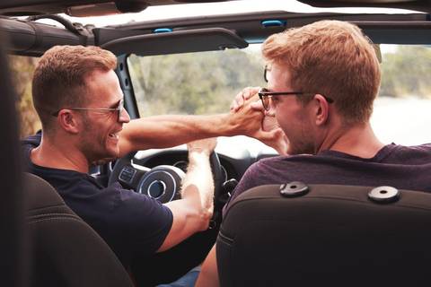 Two Male Friends Driving Open Top Car On Country Road